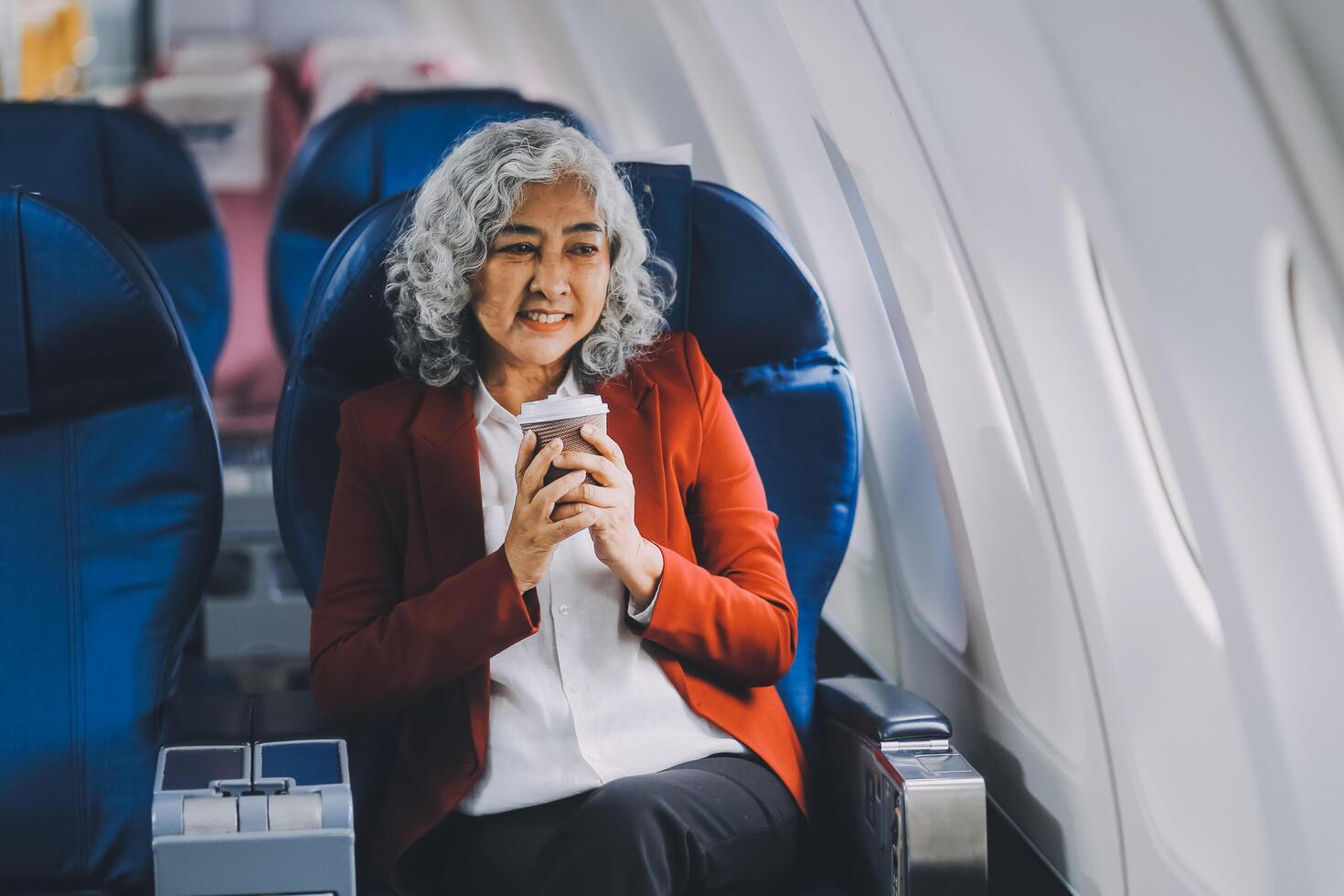 Portrait of a successful Asian businesswoman or entrepreneur in a formal suit on an airplane sitting in business class using a phone, computer laptop. Travel in style, work with grace. photo