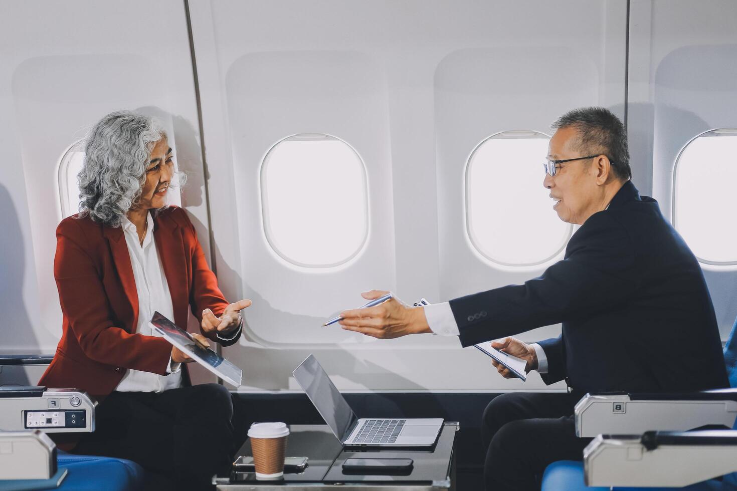 Two passengers looking at laptop together on board. Businessman in brown suit showing project on notebook to businessman with eyeglasses. Work and travel concept. photo