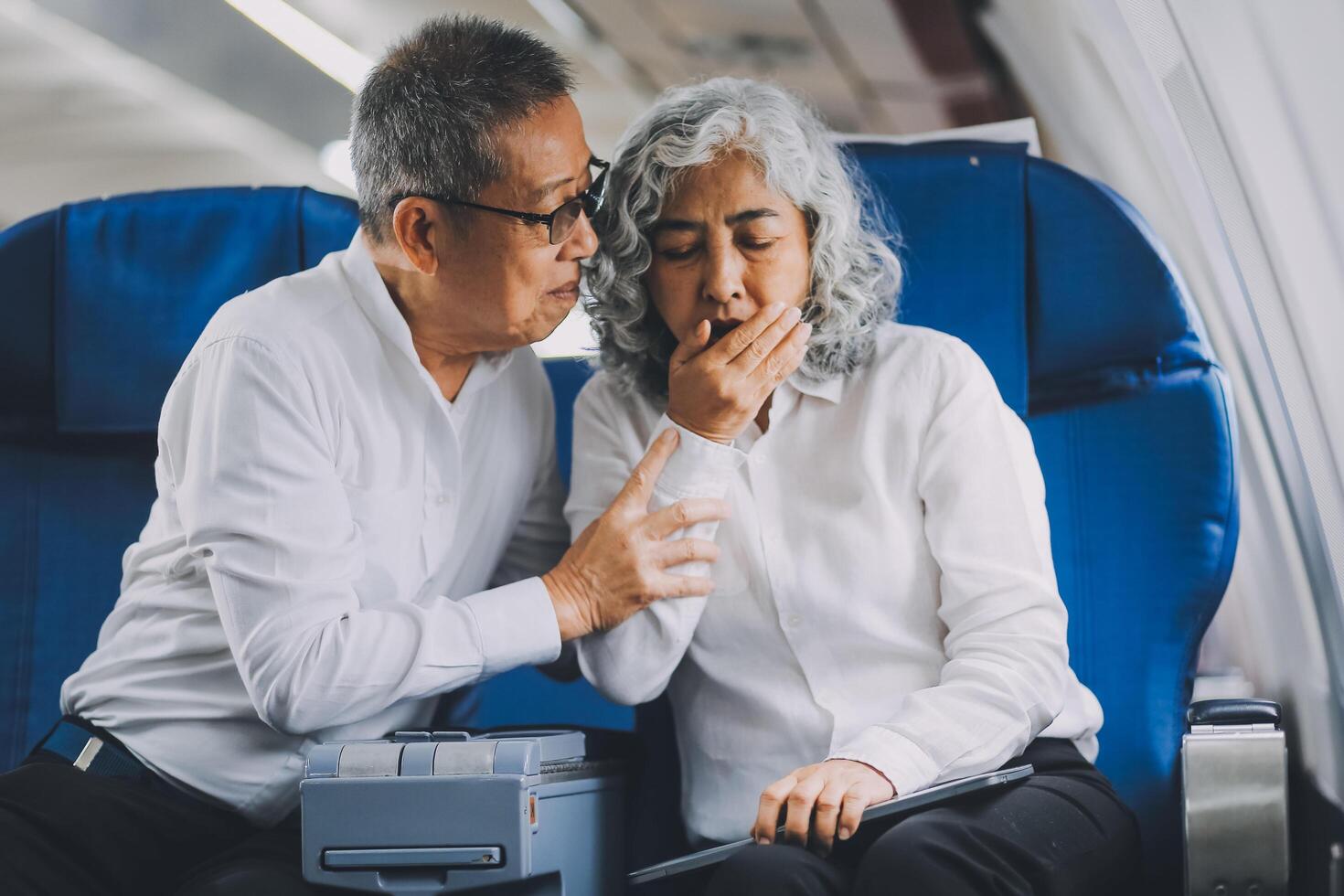 A mature woman sits by the window on a passenger plane, traveling abroad. She looks unwell, experiencing a headache, nausea, and vomiting, which dampens her travel excitement. photo