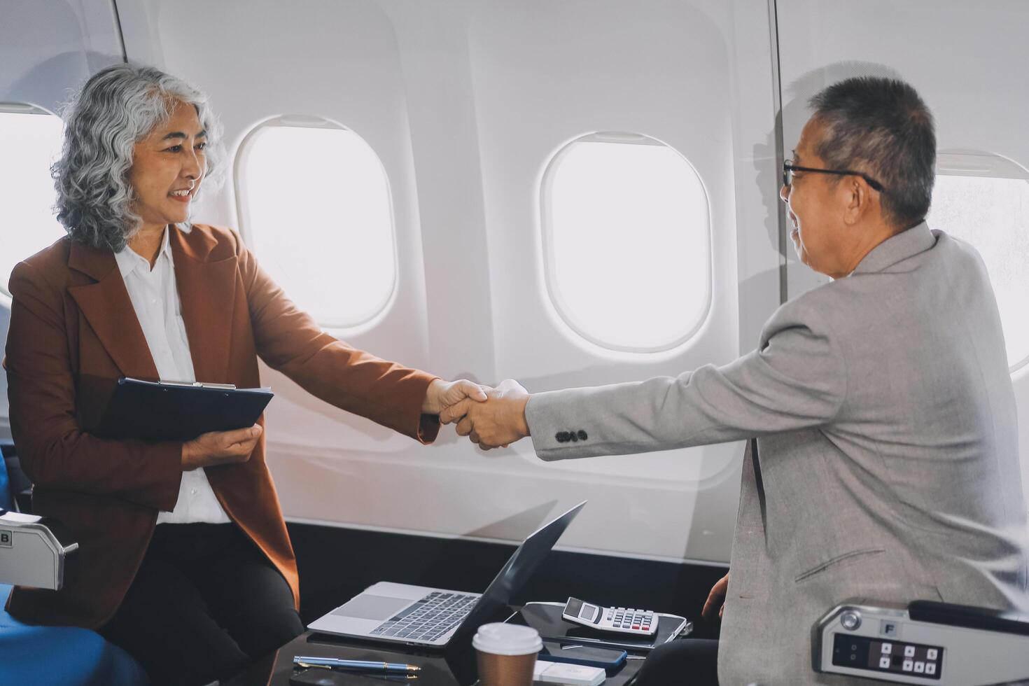 business people at meeting in private plane, Asian businessman in suit is talking to woman in jet and pointing at blank laptop screen, colleagues are discussing deal and flying in plane photo
