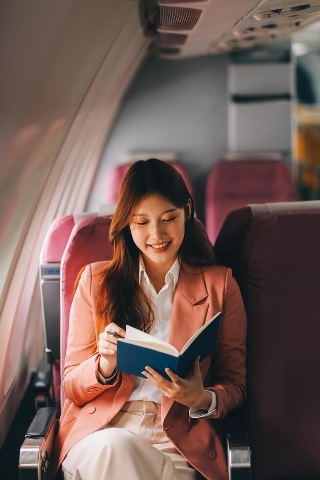 Attractive Asian female passenger of airplane sitting in comfortable seat while working laptop and tablet with mock up area using wireless connection. Travel in style, work with grace. photo