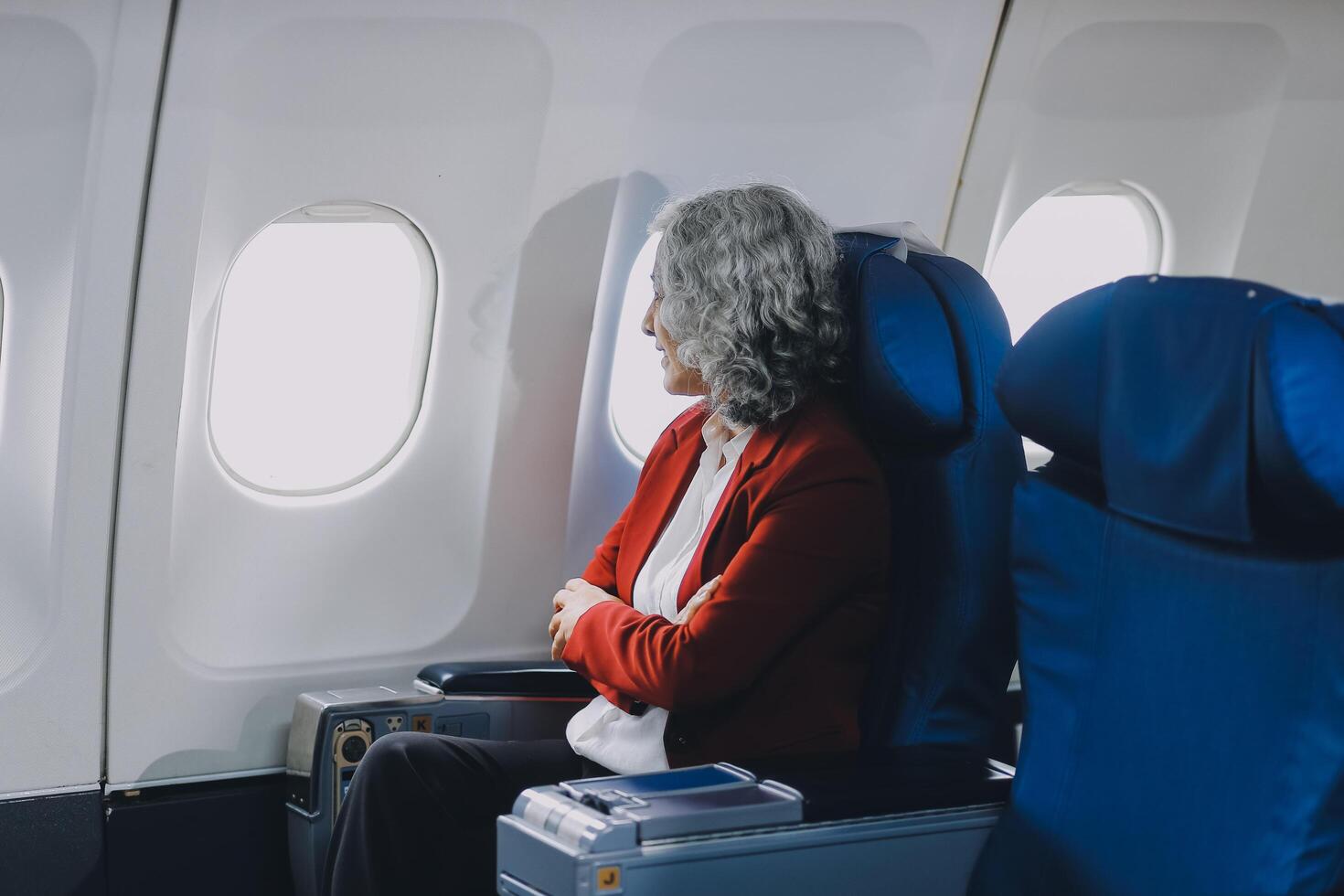 Portrait of a successful Asian businesswoman or entrepreneur in a formal suit on an airplane sitting in business class using a phone, computer laptop. Travel in style, work with grace. photo