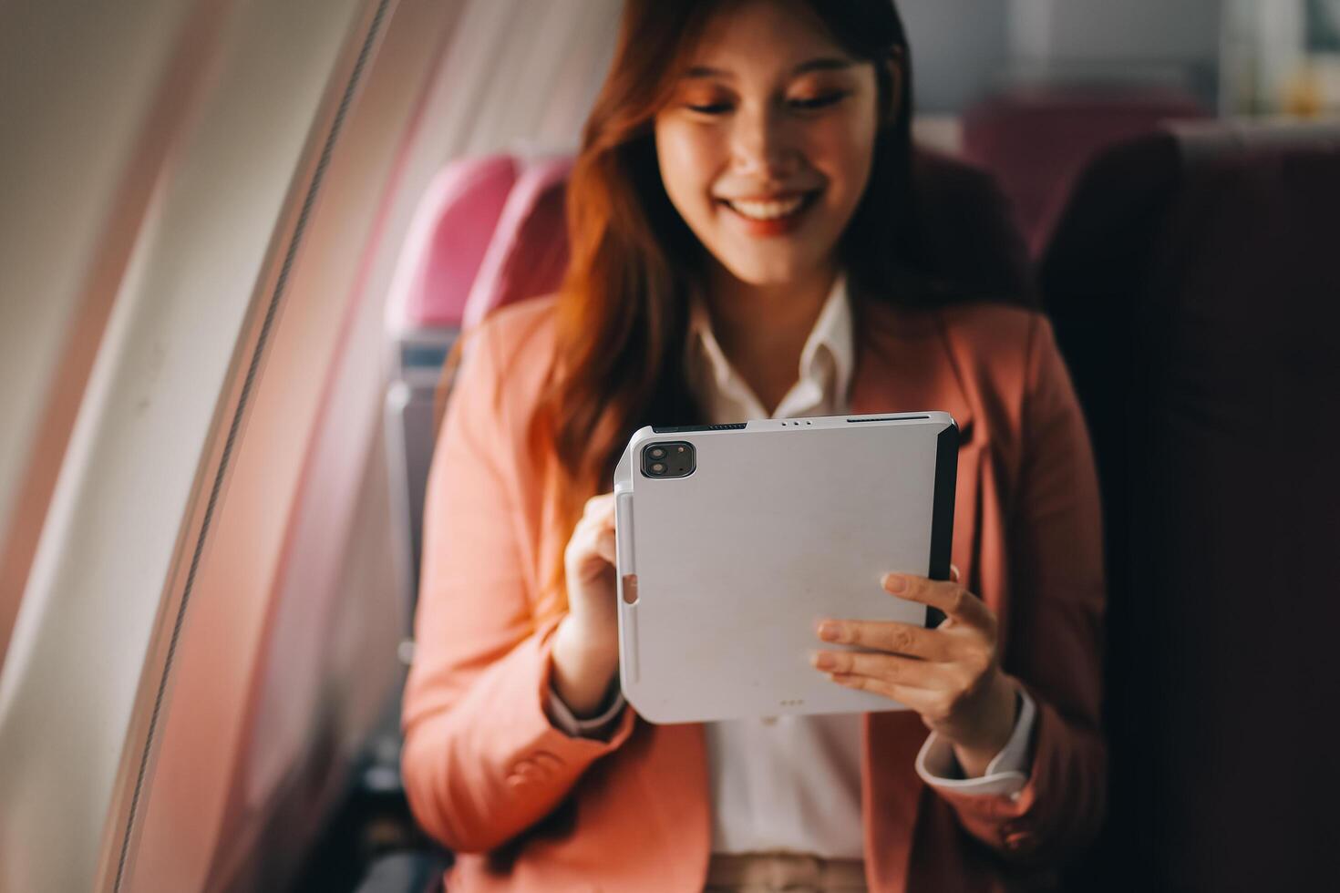 Attractive Asian female passenger of airplane sitting in comfortable seat while working laptop and tablet with mock up area using wireless connection. Travel in style, work with grace. photo