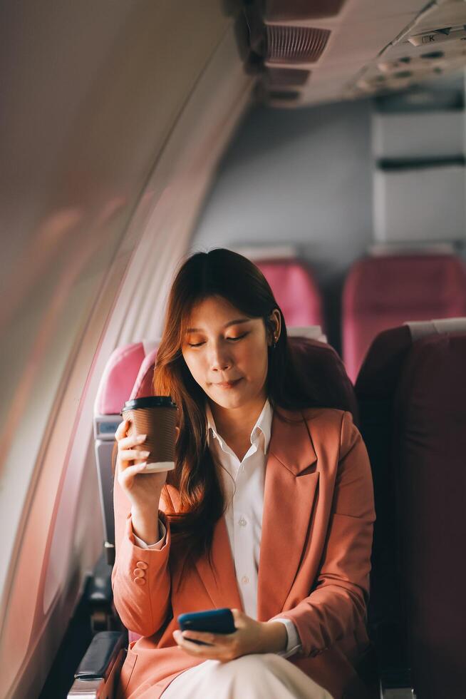 Attractive Asian female passenger of airplane sitting in comfortable seat while working laptop and tablet with mock up area using wireless connection. Travel in style, work with grace. photo