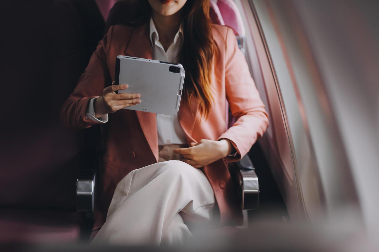 Attractive Asian female passenger of airplane sitting in comfortable seat while working laptop and tablet with mock up area using wireless connection. Travel in style, work with grace. photo