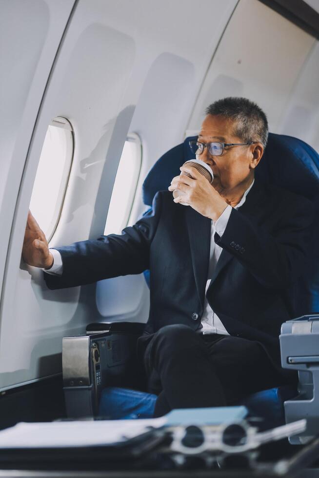 Attractive Asian male passenger of airplane sitting in comfortable seat while working laptop and tablet with mock up area using wireless connection. Travel in style, work with grace. photo