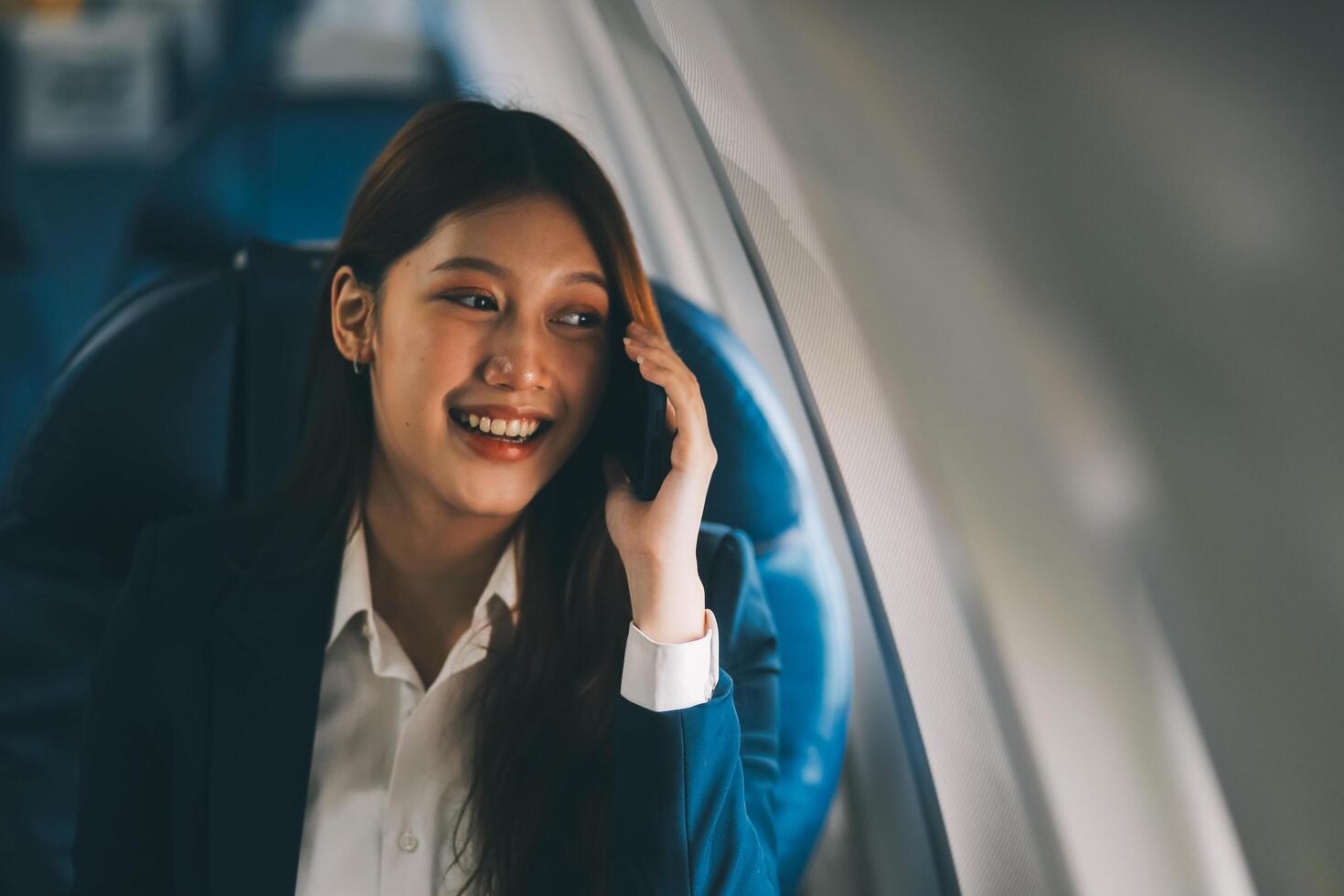 A young Asian female airplane passenger sits by the window during the flight, holding her boarding pass, with her carry-on luggage stored overhead, wearing her seatbelt, and enjoying the journey. photo