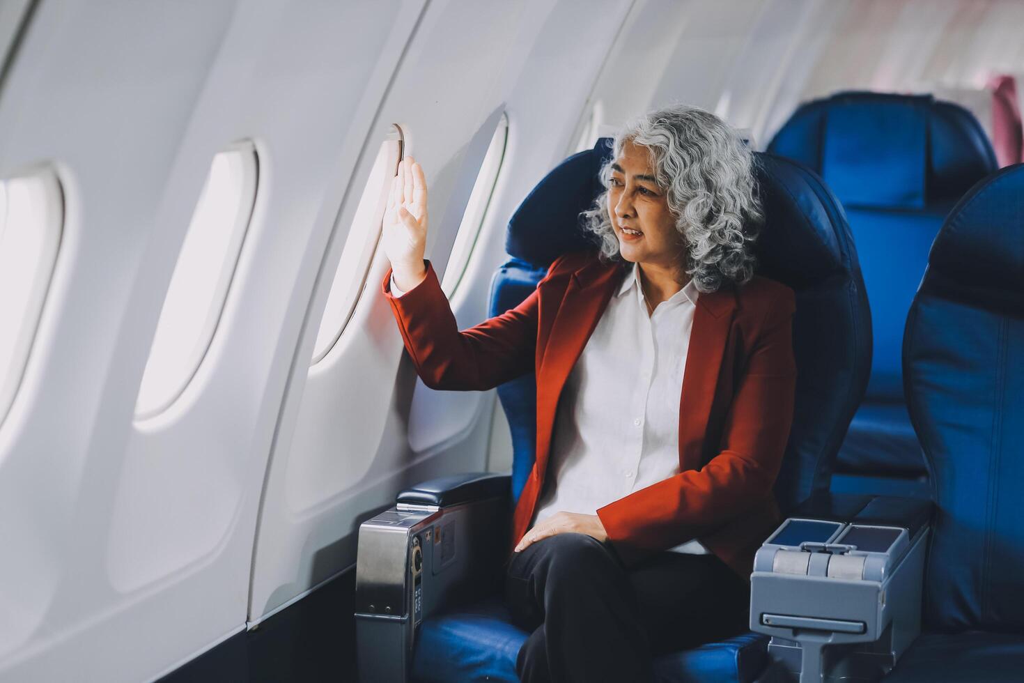 Portrait of a successful Asian businesswoman or entrepreneur in a formal suit on an airplane sitting in business class using a phone, computer laptop. Travel in style, work with grace. photo