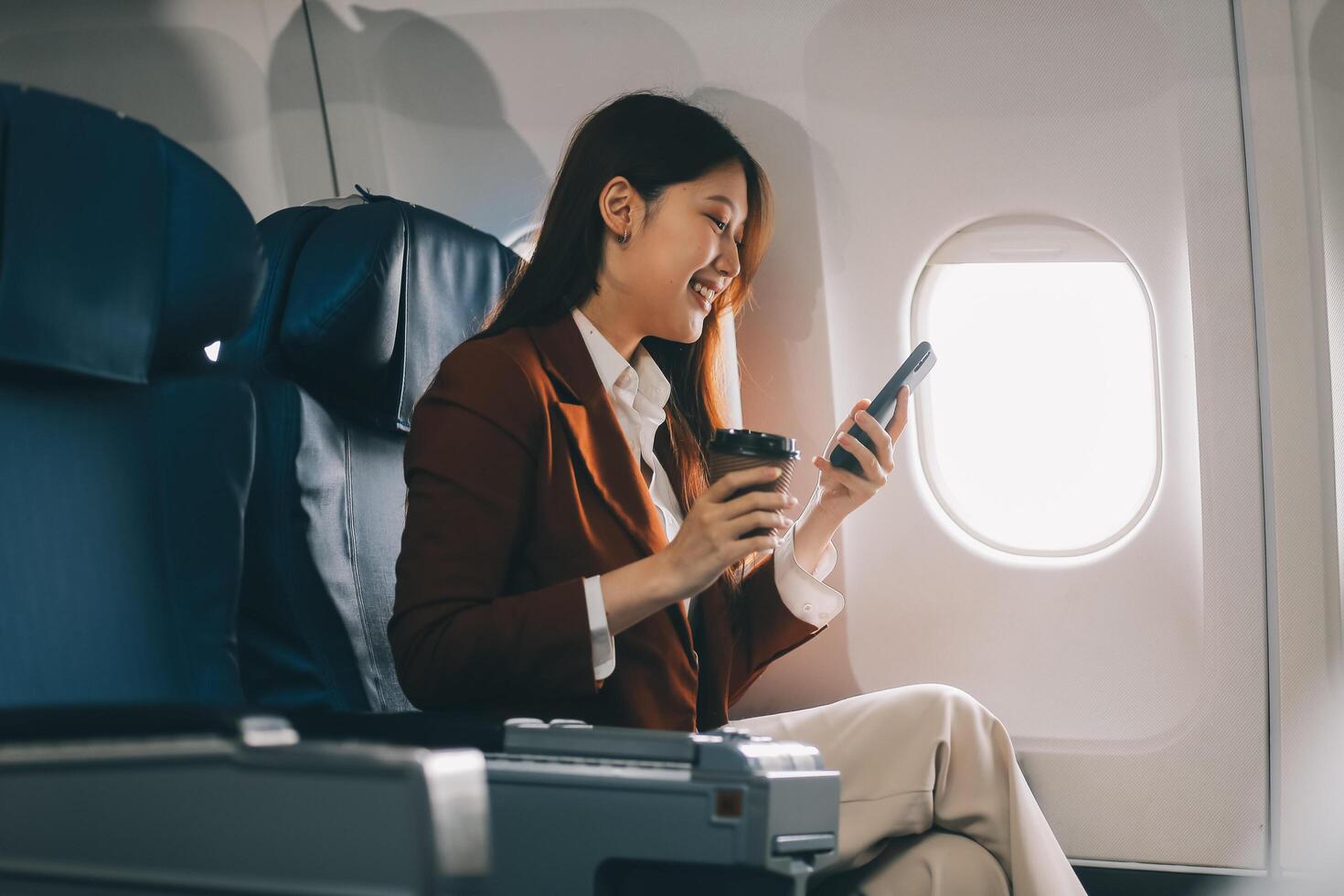 Asian woman looking at phone while sitting on airplane Technology female travelers using mobile smartphones, online apps, and the internet while sitting in airplane seats during travel. photo
