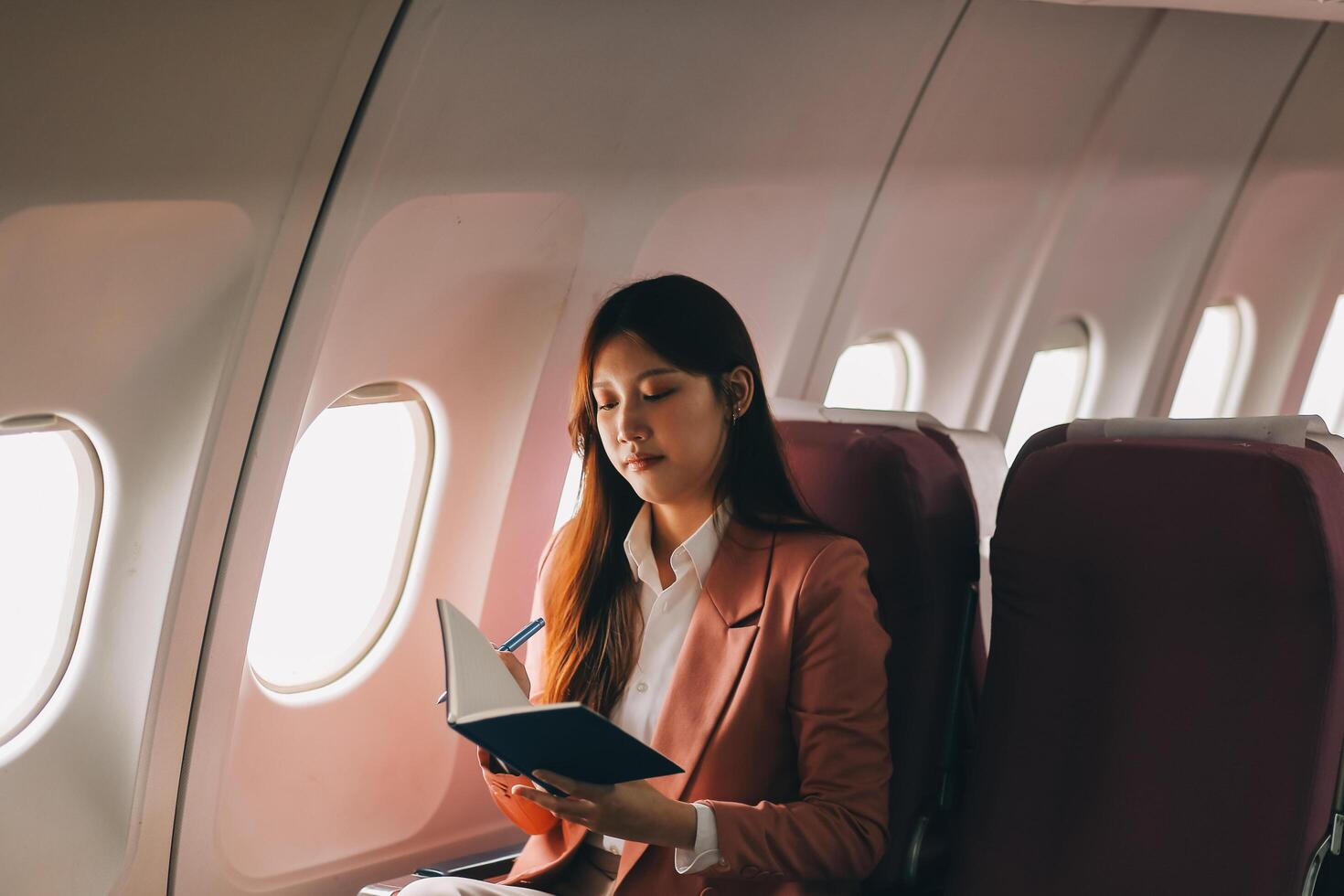 Attractive Asian female passenger of airplane sitting in comfortable seat while working laptop and tablet with mock up area using wireless connection. Travel in style, work with grace. photo