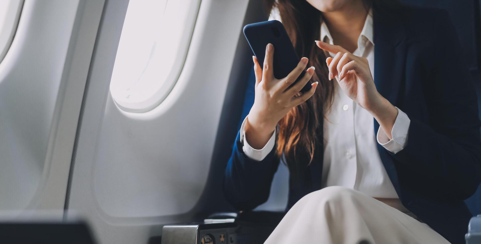A young Asian female airplane passenger sits by the window during the flight, holding her boarding pass, with her carry-on luggage stored overhead, wearing her seatbelt, and enjoying the journey. photo
