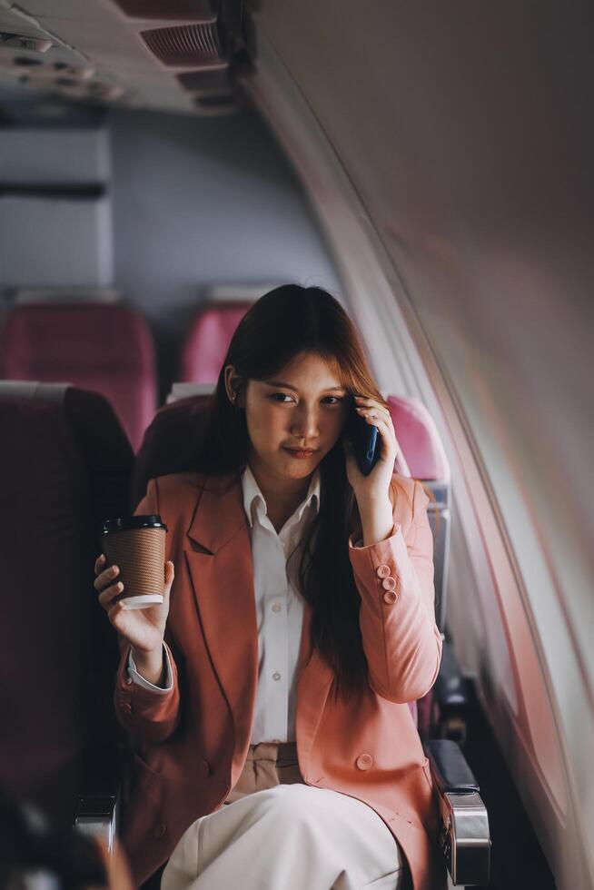 Attractive Asian female passenger of airplane sitting in comfortable seat while working laptop and tablet with mock up area using wireless connection. Travel in style, work with grace. photo