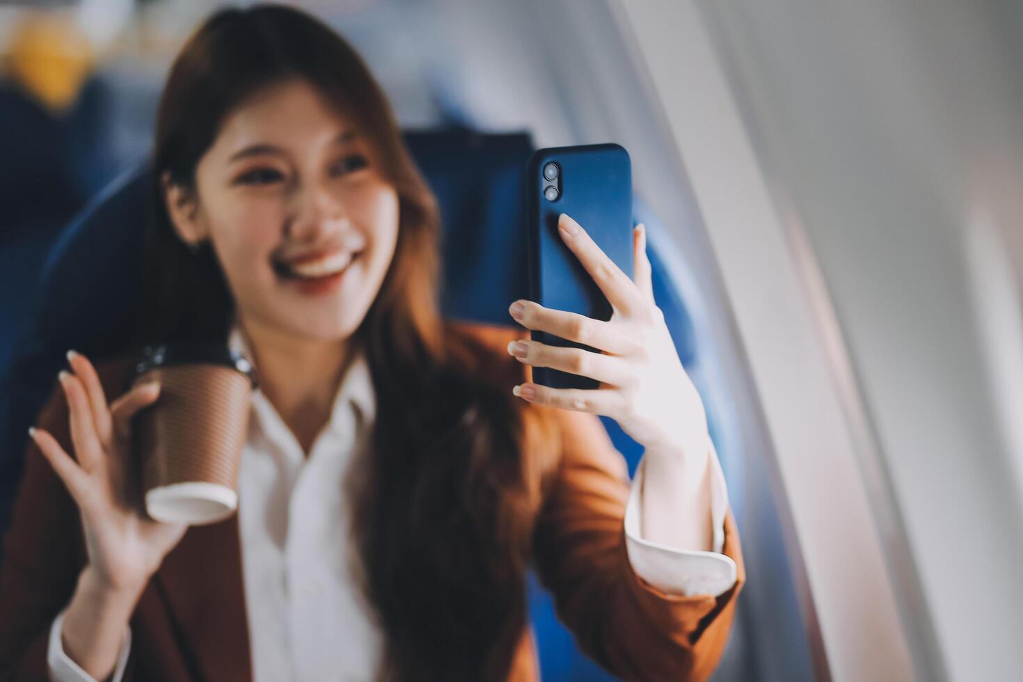 Asian woman looking at phone while sitting on airplane Technology female travelers using mobile smartphones, online apps, and the internet while sitting in airplane seats during travel. photo
