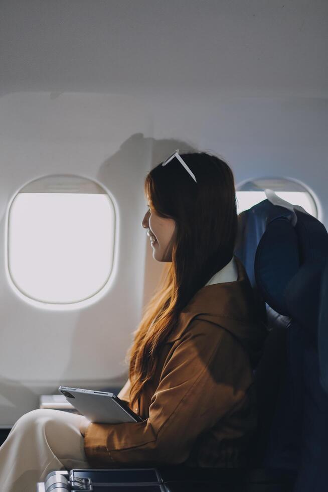 Joyful asian woman sits in the airplane and using tablet while go to travel photo