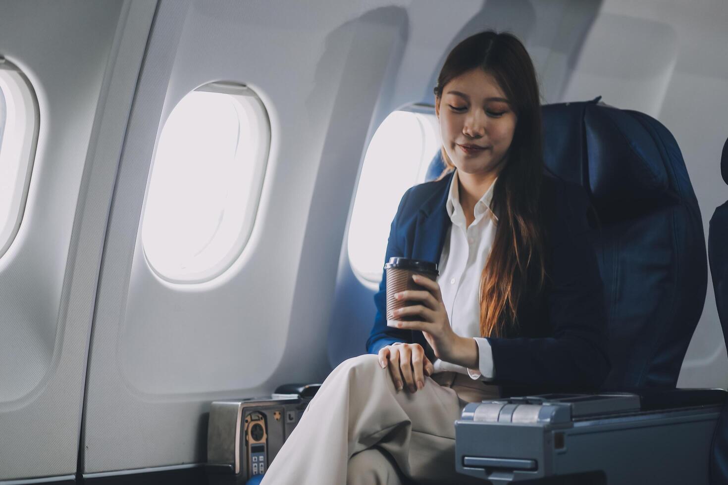 Young Asian female tourist traveling alone on a plane is drinking hot coffee and looking out the window. photo