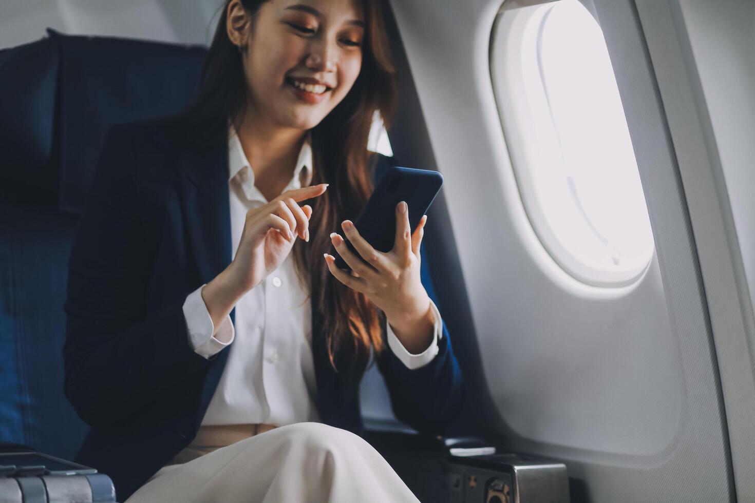 A young Asian female airplane passenger sits by the window during the flight, holding her boarding pass, with her carry-on luggage stored overhead, wearing her seatbelt, and enjoying the journey. photo