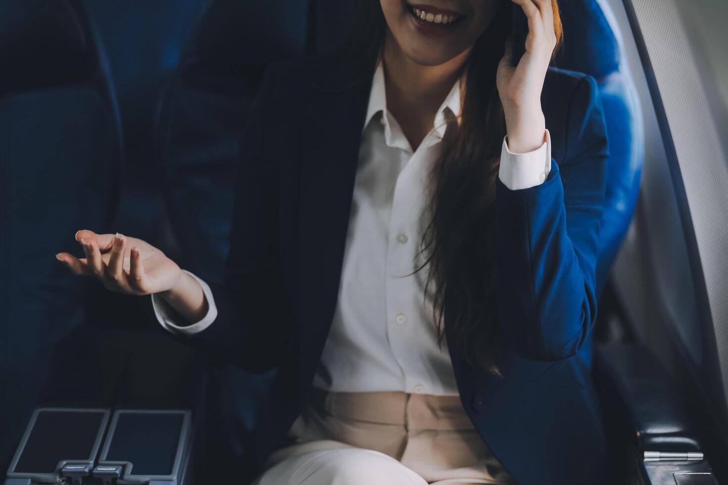 A young Asian female airplane passenger sits by the window during the flight, holding her boarding pass, with her carry-on luggage stored overhead, wearing her seatbelt, and enjoying the journey. photo