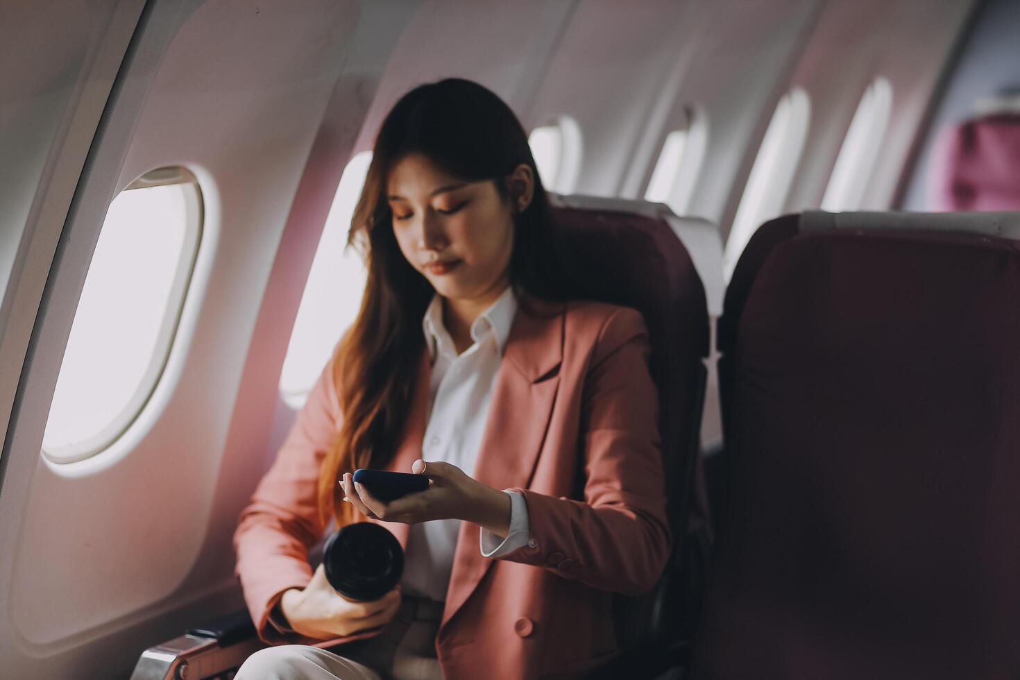 Attractive Asian female passenger of airplane sitting in comfortable seat while working laptop and tablet with mock up area using wireless connection. Travel in style, work with grace. photo