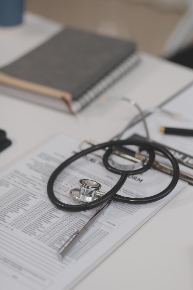 Doctor's working on laptop computer, writing prescription clipboard with record information paper folders on desk in hospital or clinic, Healthcare and medical concept. Focus on stethoscope photo