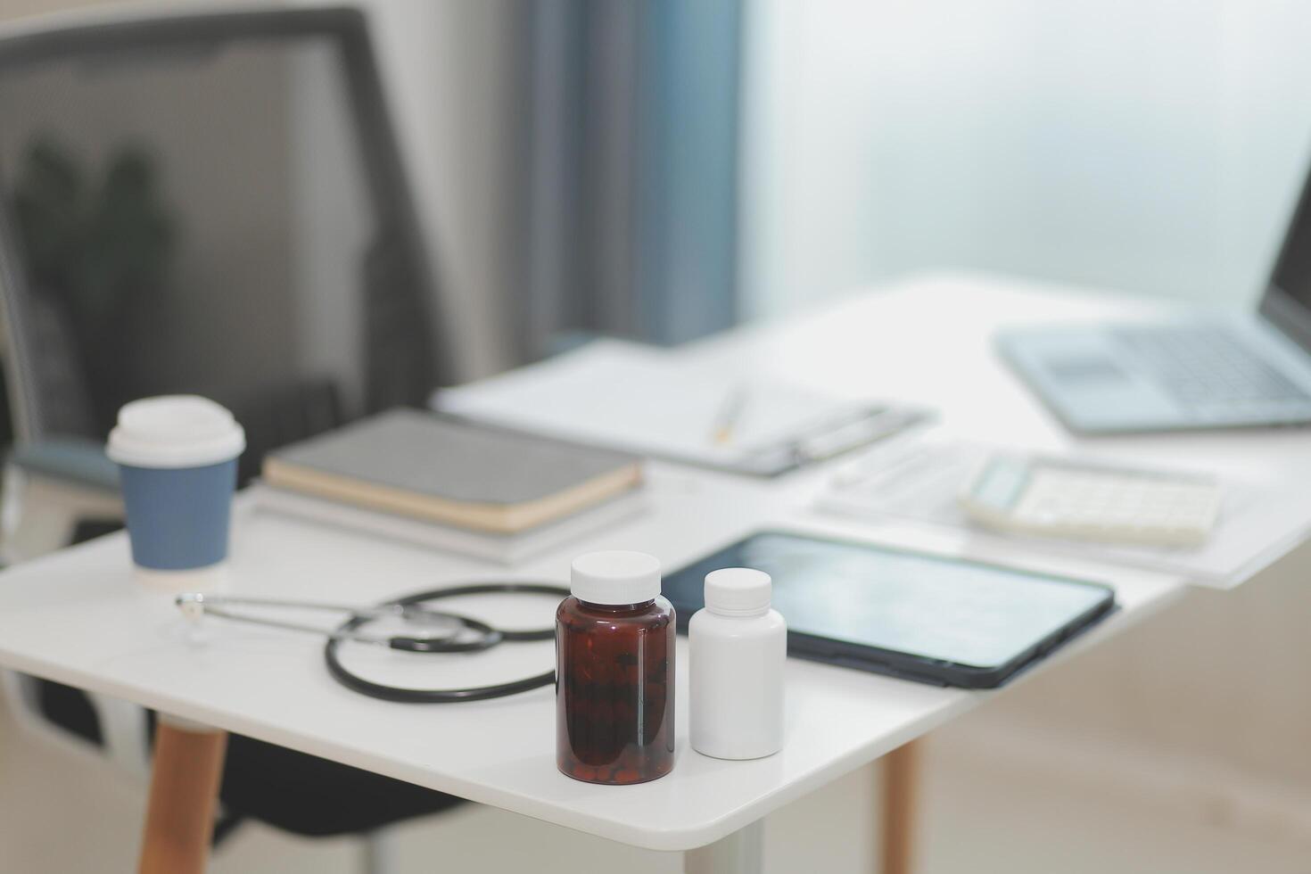 Doctor's working on laptop computer, writing prescription clipboard with record information paper folders on desk in hospital or clinic, Healthcare and medical concept. Focus on stethoscope photo