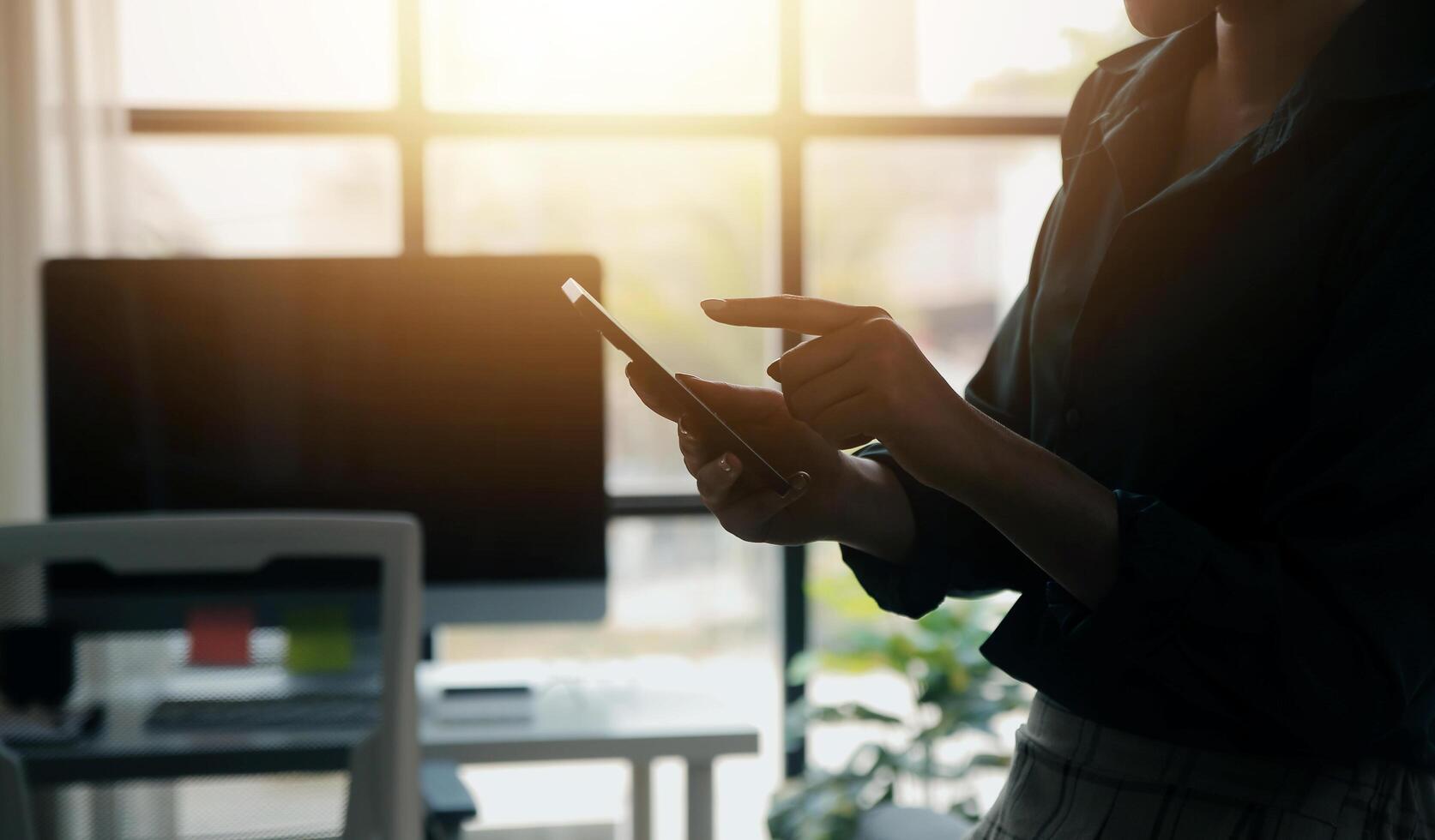Smiling businesswoman using her phone in the office. Small business entrepreneur looking at her mobile phone and smiling while communicating with her office colleagues photo