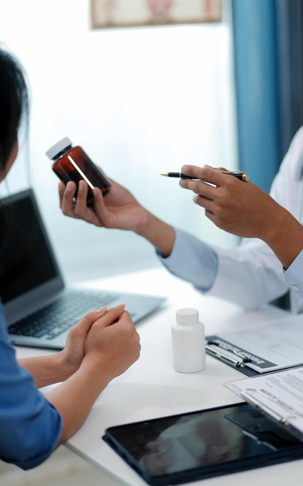 Doctor and patient sitting near each other at the wooden desk in clinic. Female physician's pointing to a records form. Medicine concept photo