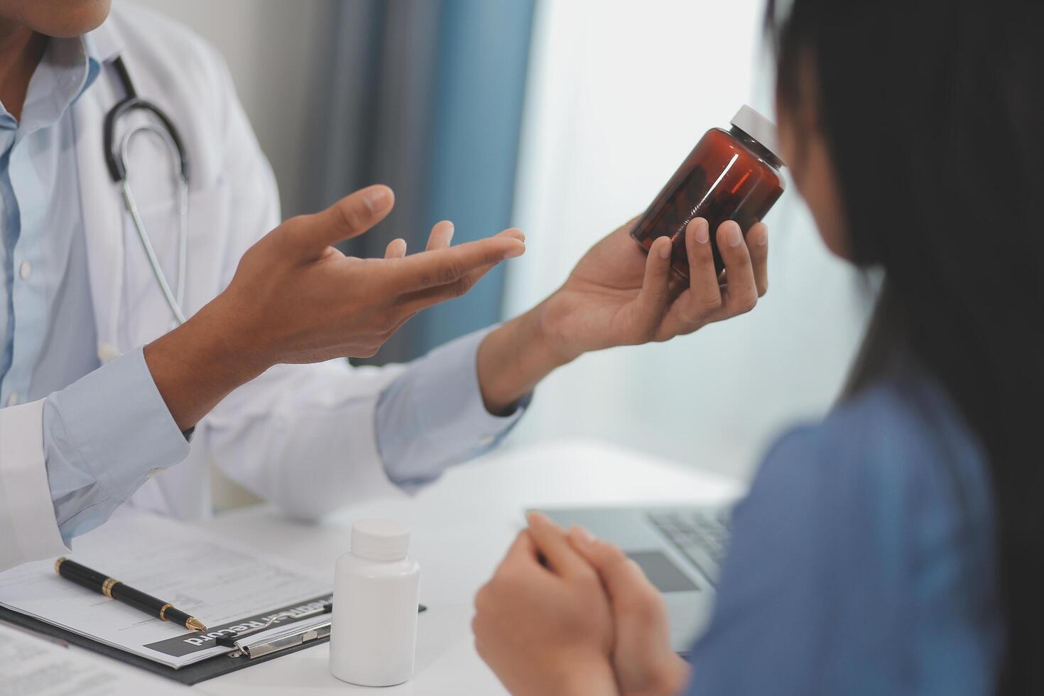 Doctor and patient sitting near each other at the wooden desk in clinic. Female physician's pointing to a records form. Medicine concept photo