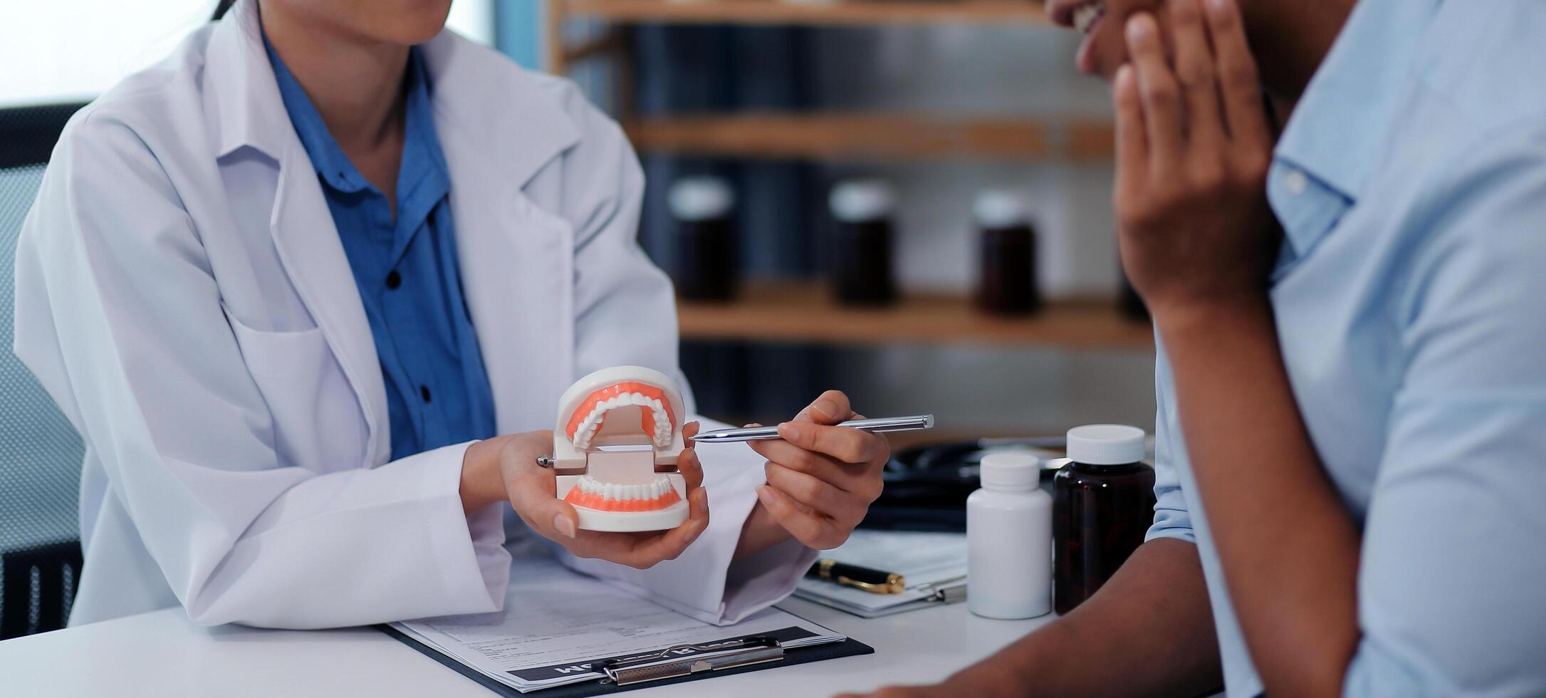 Dentist consultation - patient visit at the dental clinic office. Female dentist wearing dentures to explain teeth Recommend guidelines for orthodontics Dentist giving advice on patient's condition photo