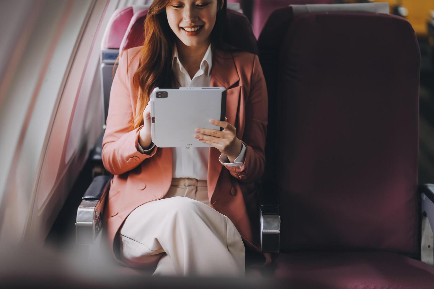 Attractive Asian female passenger of airplane sitting in comfortable seat while working laptop and tablet with mock up area using wireless connection. Travel in style, work with grace. photo