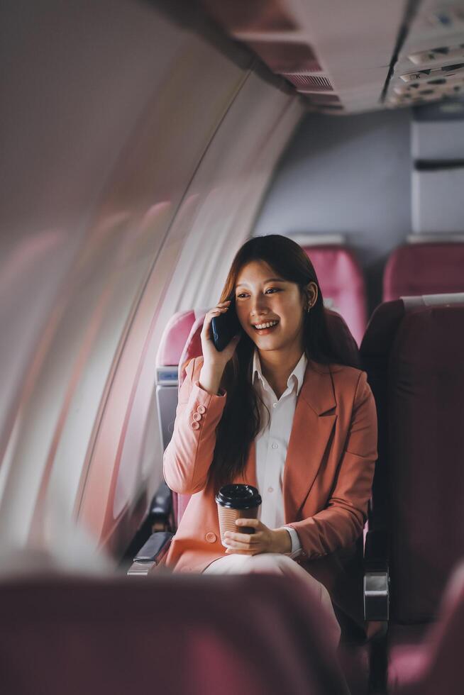 Attractive Asian female passenger of airplane sitting in comfortable seat while working laptop and tablet with mock up area using wireless connection. Travel in style, work with grace. photo