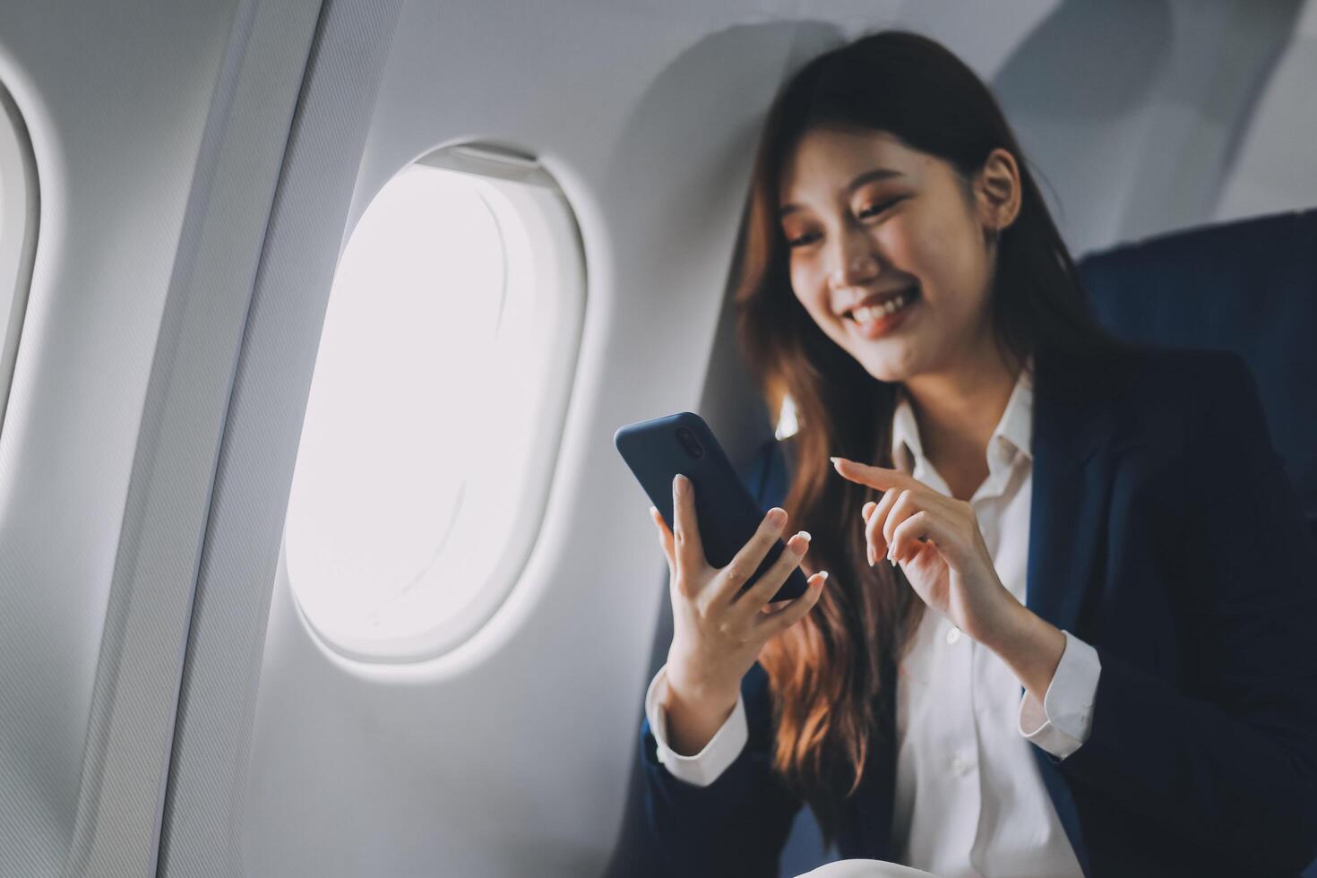 A young Asian female airplane passenger sits by the window during the flight, holding her boarding pass, with her carry-on luggage stored overhead, wearing her seatbelt, and enjoying the journey. photo