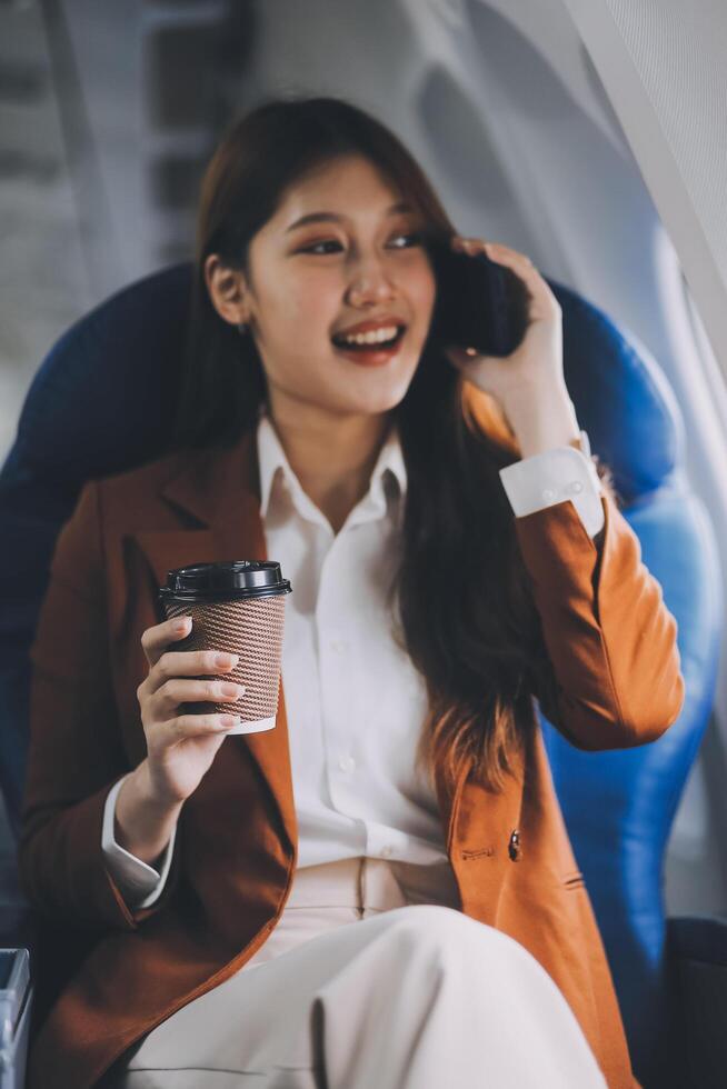 Asian woman looking at phone while sitting on airplane Technology female travelers using mobile smartphones, online apps, and the internet while sitting in airplane seats during travel. photo