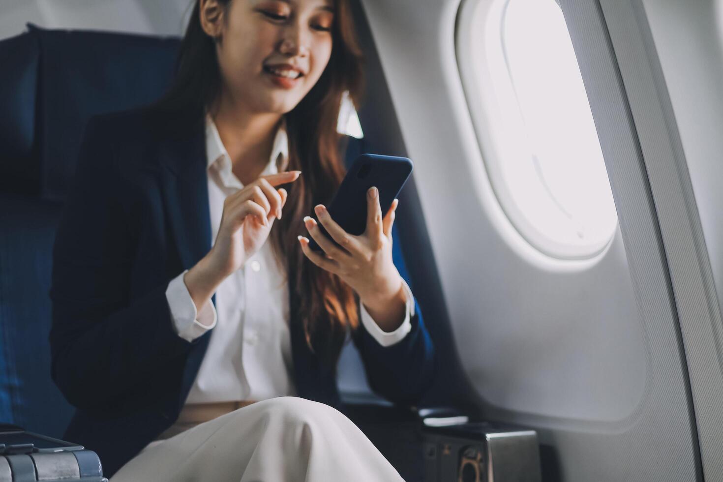 A young Asian female airplane passenger sits by the window during the flight, holding her boarding pass, with her carry-on luggage stored overhead, wearing her seatbelt, and enjoying the journey. photo