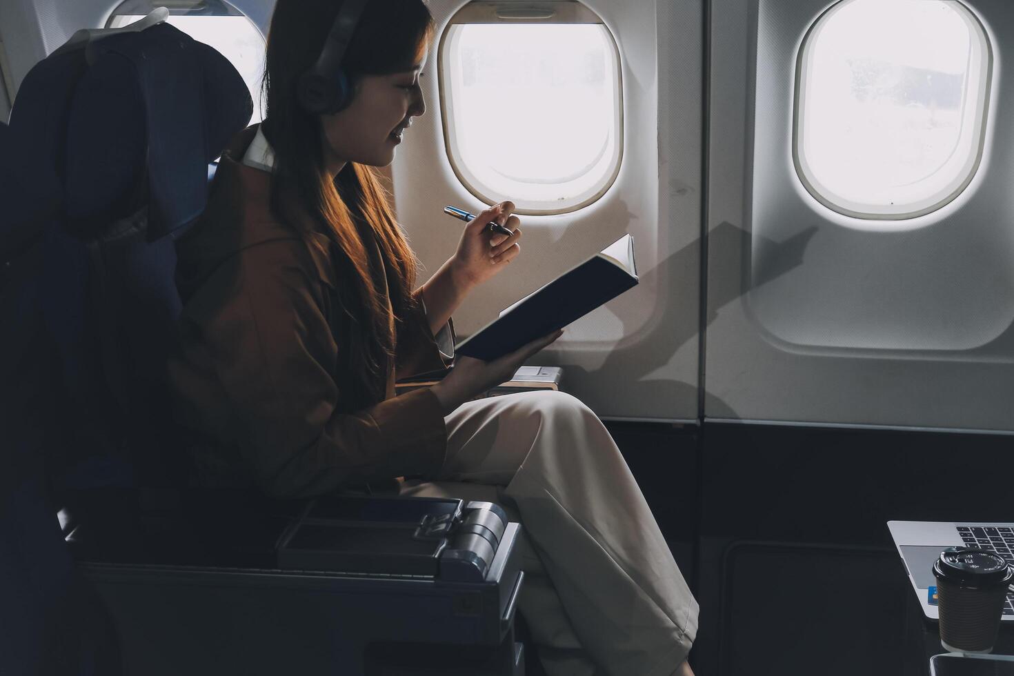 A young Asian woman, seated as an airplane passenger, contemplates dollar bills, reflecting on lucrative opportunities and aspirations towards billionaire status. photo