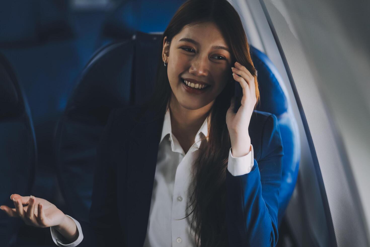 A young Asian female airplane passenger sits by the window during the flight, holding her boarding pass, with her carry-on luggage stored overhead, wearing her seatbelt, and enjoying the journey. photo