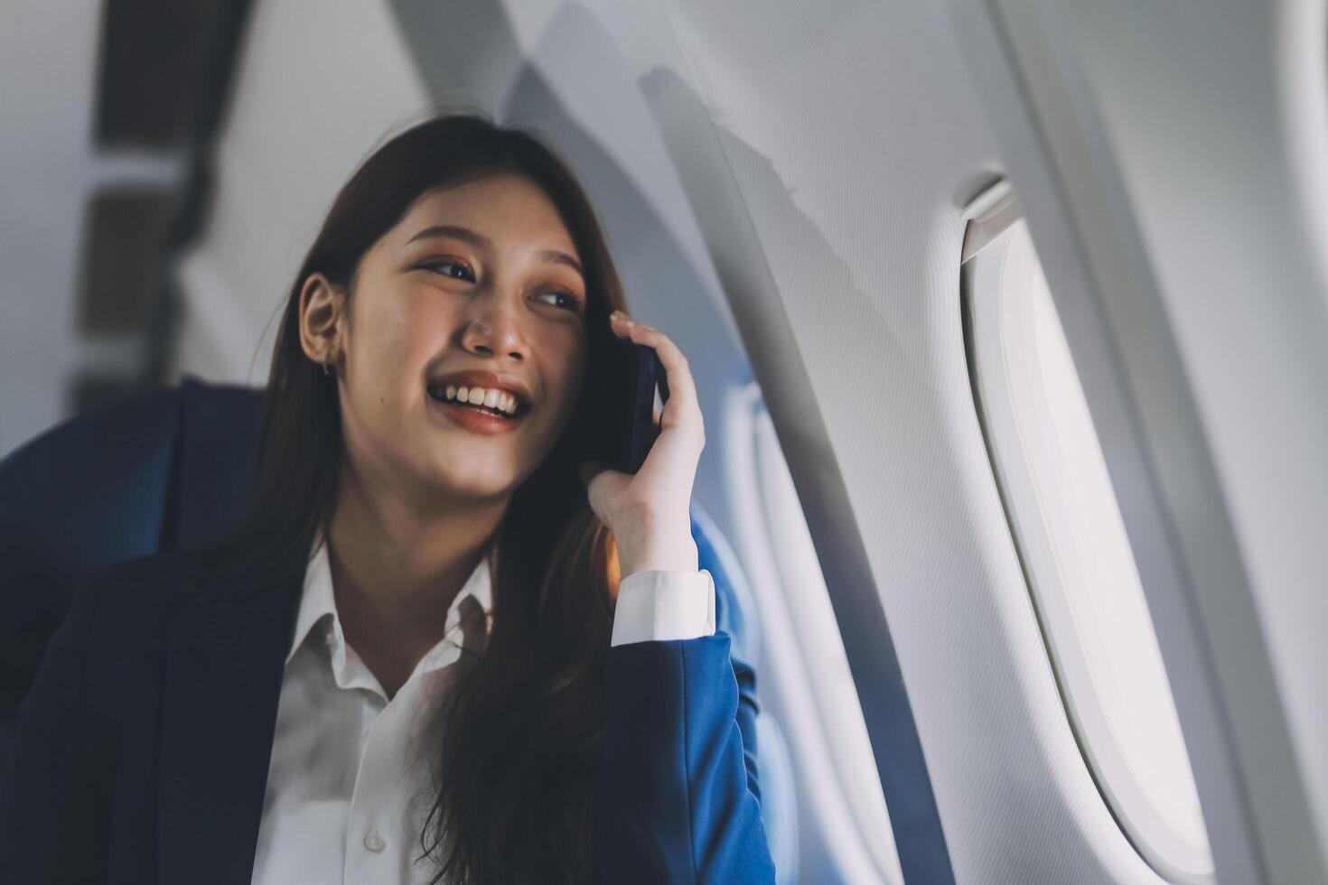 A young Asian female airplane passenger sits by the window during the flight, holding her boarding pass, with her carry-on luggage stored overhead, wearing her seatbelt, and enjoying the journey. photo