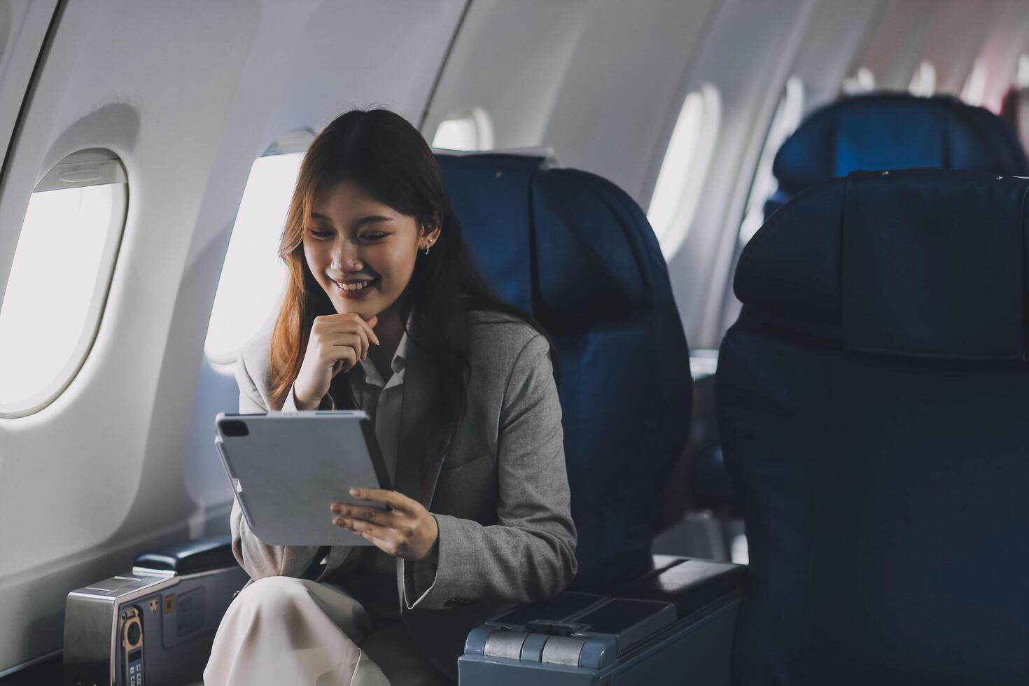Joyful asian woman sits in the airplane and using tablet while go to travel photo