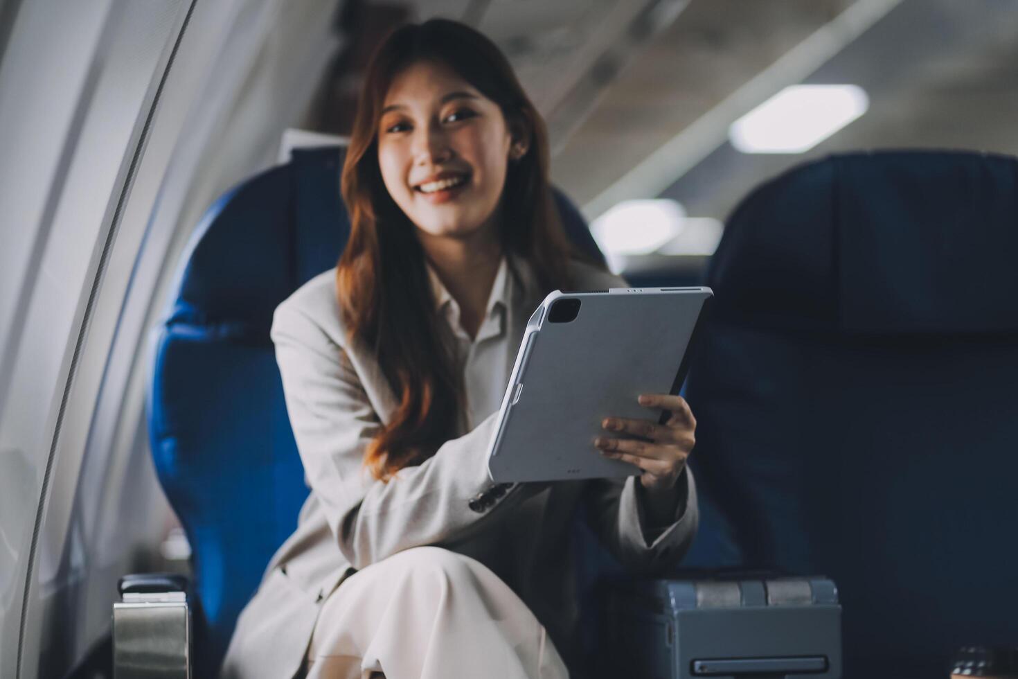 Joyful asian woman sits in the airplane and using tablet while go to travel photo