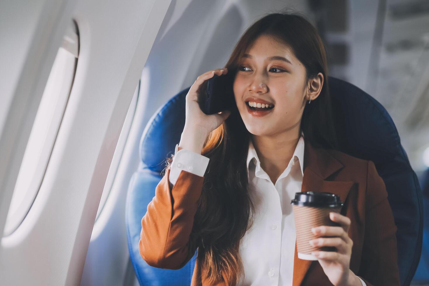 Asian woman looking at phone while sitting on airplane Technology female travelers using mobile smartphones, online apps, and the internet while sitting in airplane seats during travel. photo