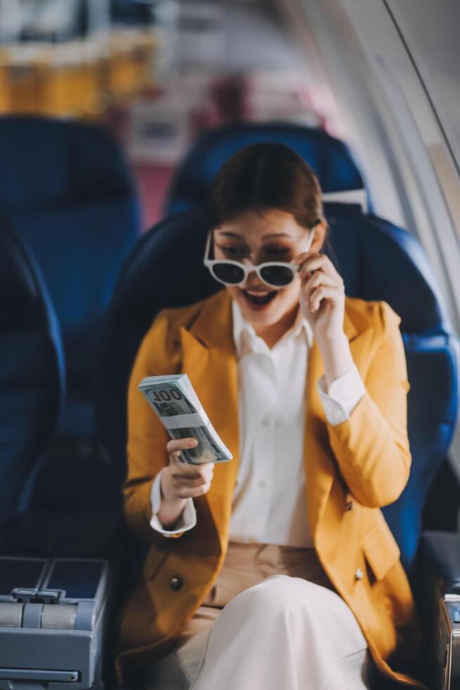 A young Asian woman, seated as an airplane passenger, contemplates dollar bills, reflecting on lucrative opportunities and aspirations towards billionaire status. photo
