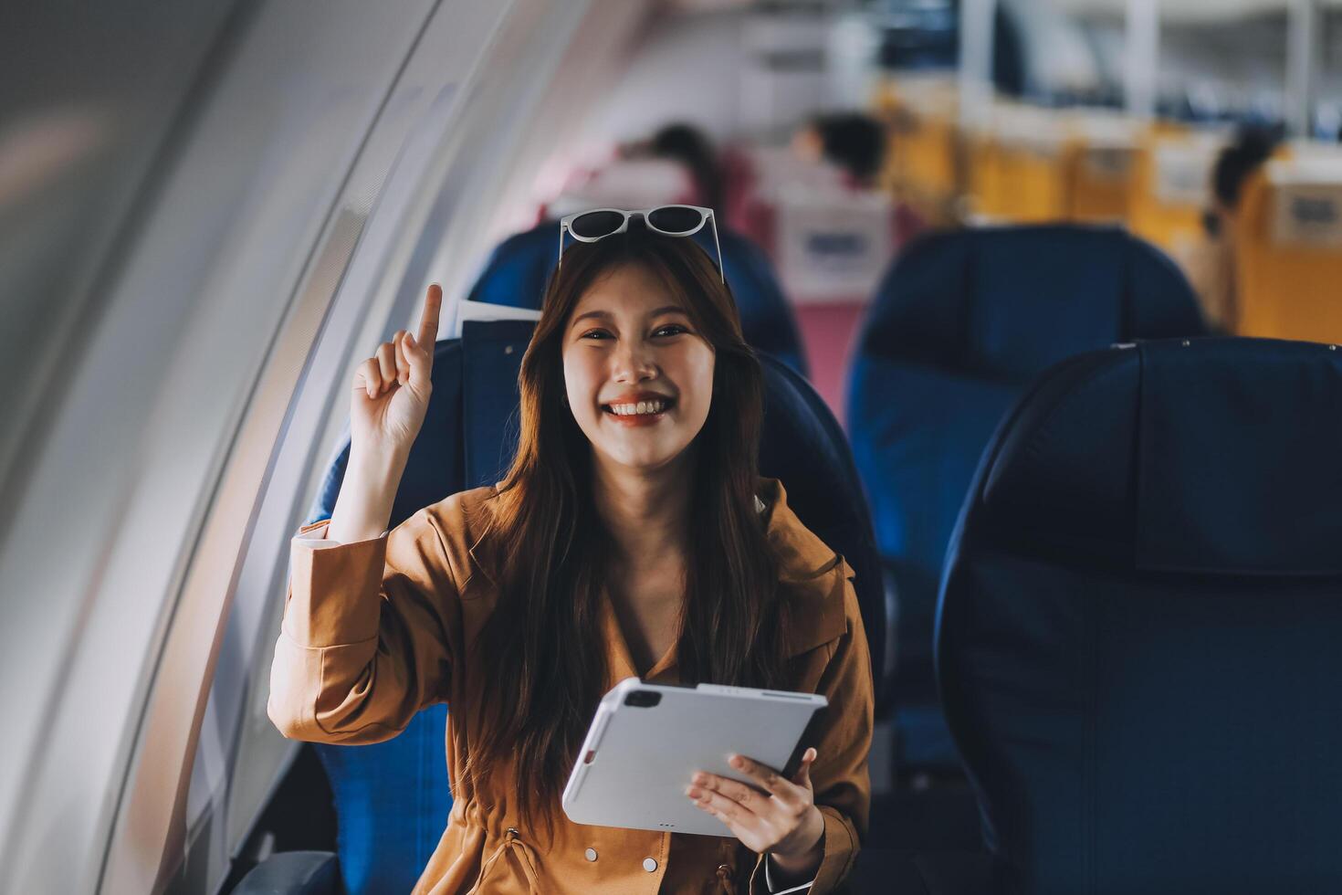 Joyful asian woman sits in the airplane and using tablet while go to travel photo