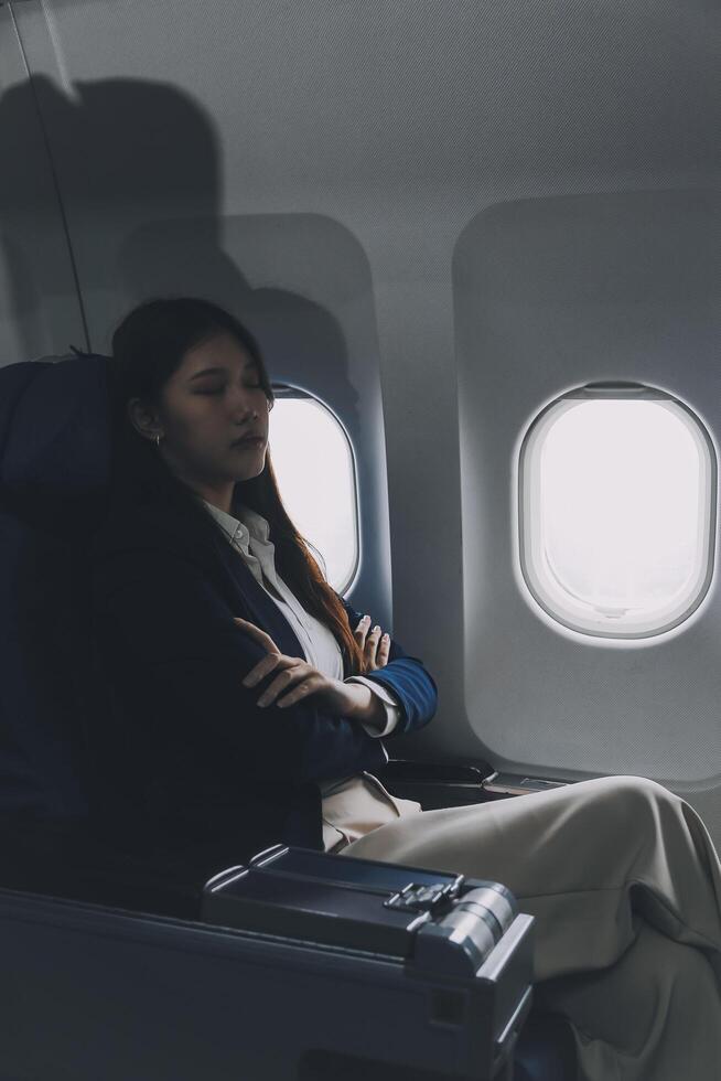 Photo of a frustrated woman sitting on an airplane with her head in her hands. Asian woman sitting in a seat in airplane