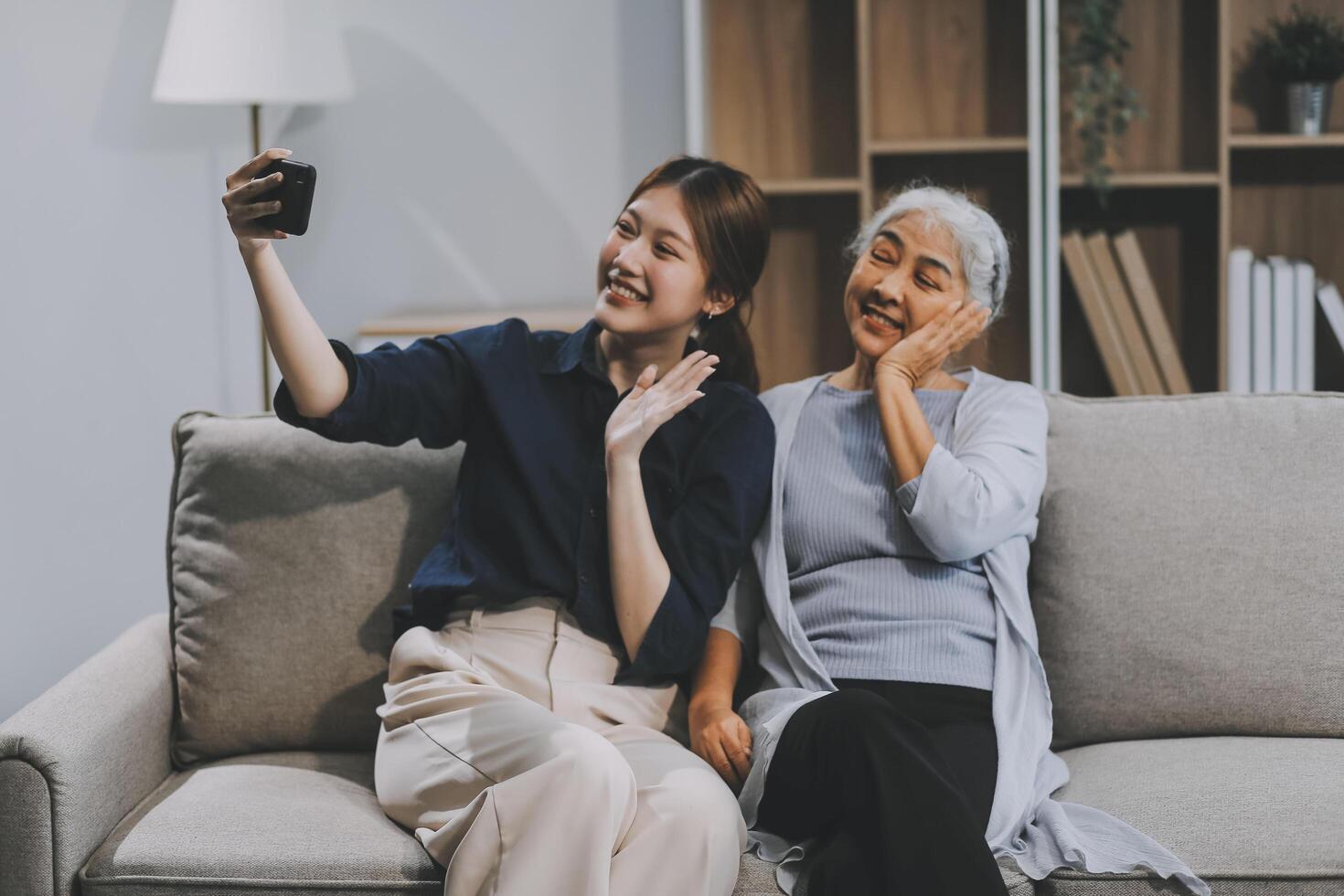 Cheerful mother and pretty teenager kid relaxing at cozy home, using mobile phone for Internet communication, resting on sofa with digital gadget, enjoying leisure, looking at camera photo