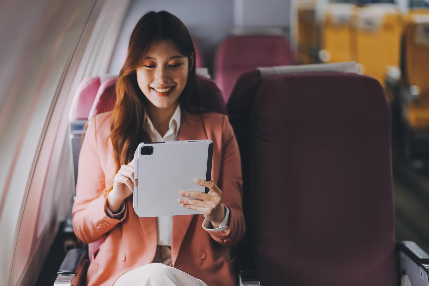 Attractive Asian female passenger of airplane sitting in comfortable seat while working laptop and tablet with mock up area using wireless connection. Travel in style, work with grace. photo