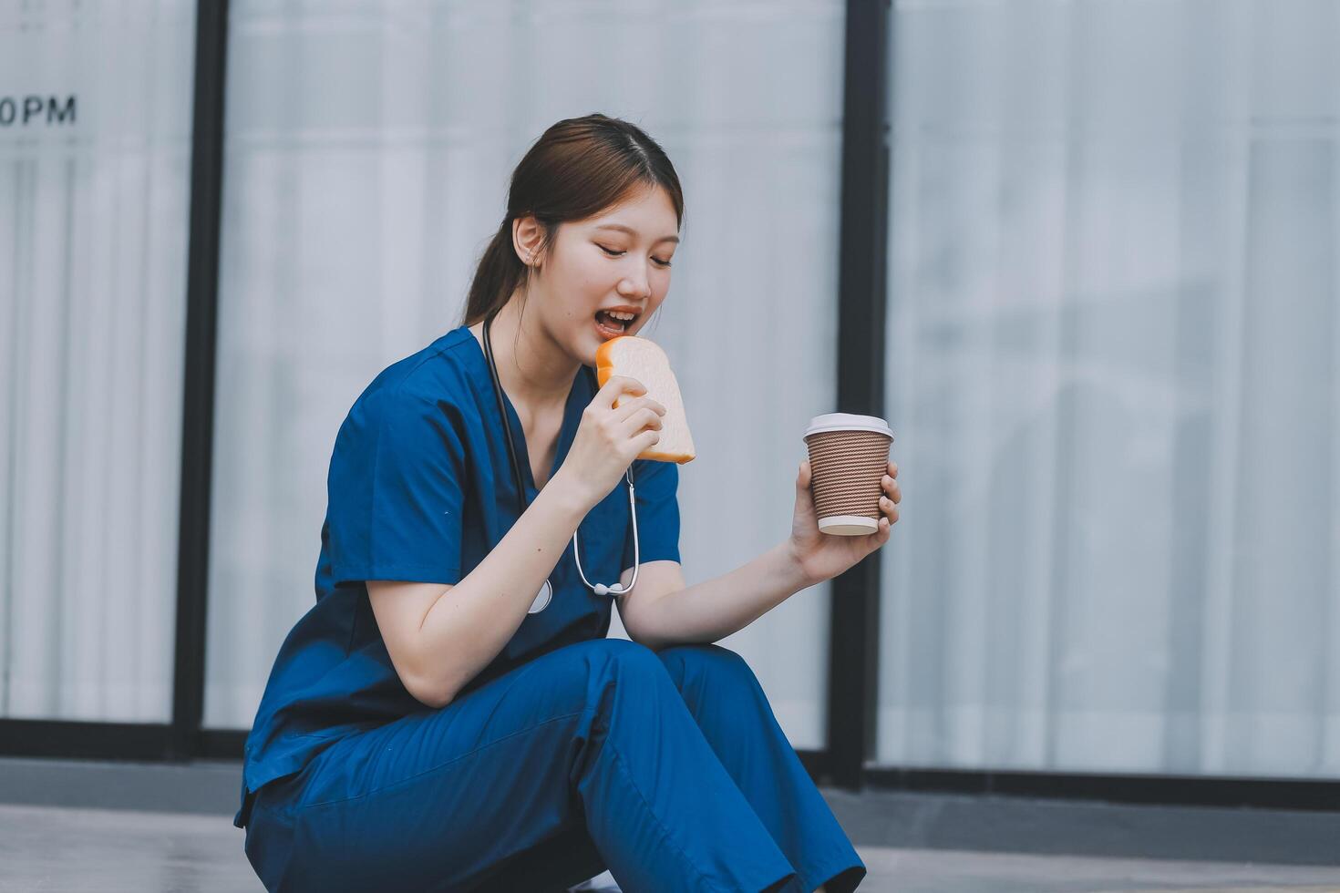 A cheerful woman in scrubs holds a clipboard, standing confidently before a modern hospital building, representing professional healthcare service. photo