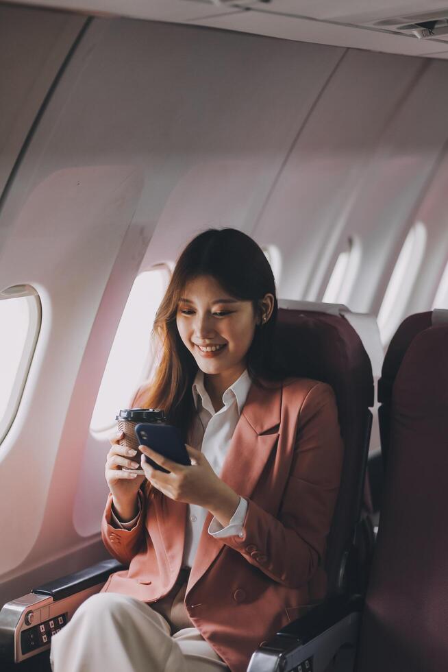 Attractive Asian female passenger of airplane sitting in comfortable seat while working laptop and tablet with mock up area using wireless connection. Travel in style, work with grace. photo