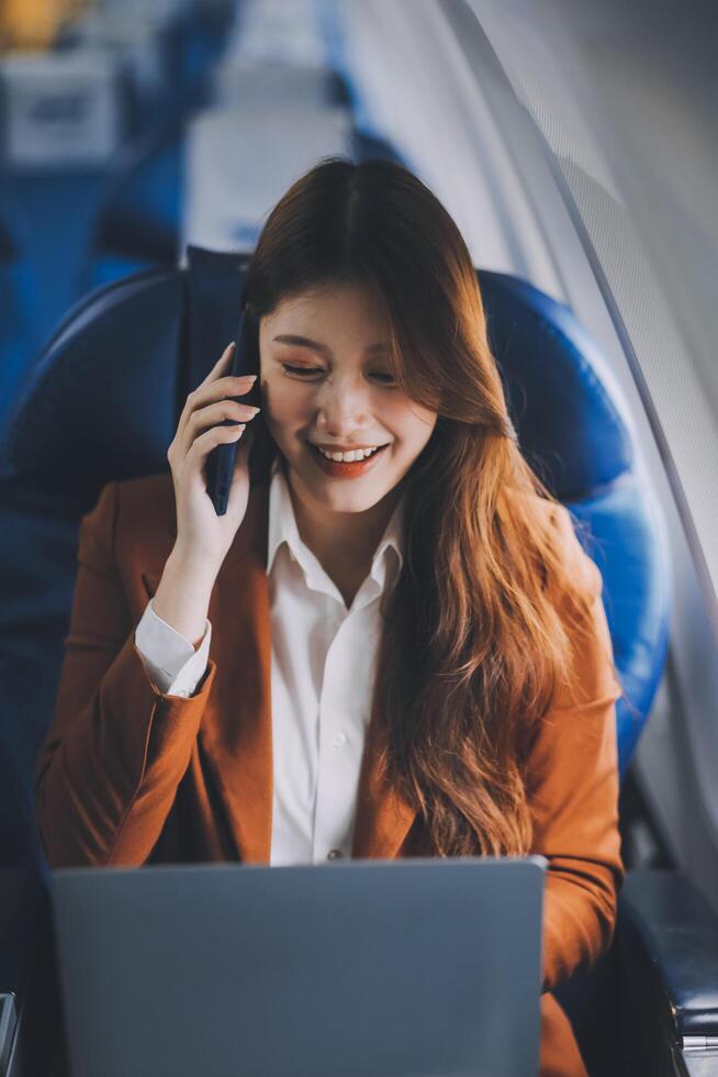 Young Asian executive excels in first class, multitasking with digital tablet, laptop and smartphone. Travel in style, work with grace. photo