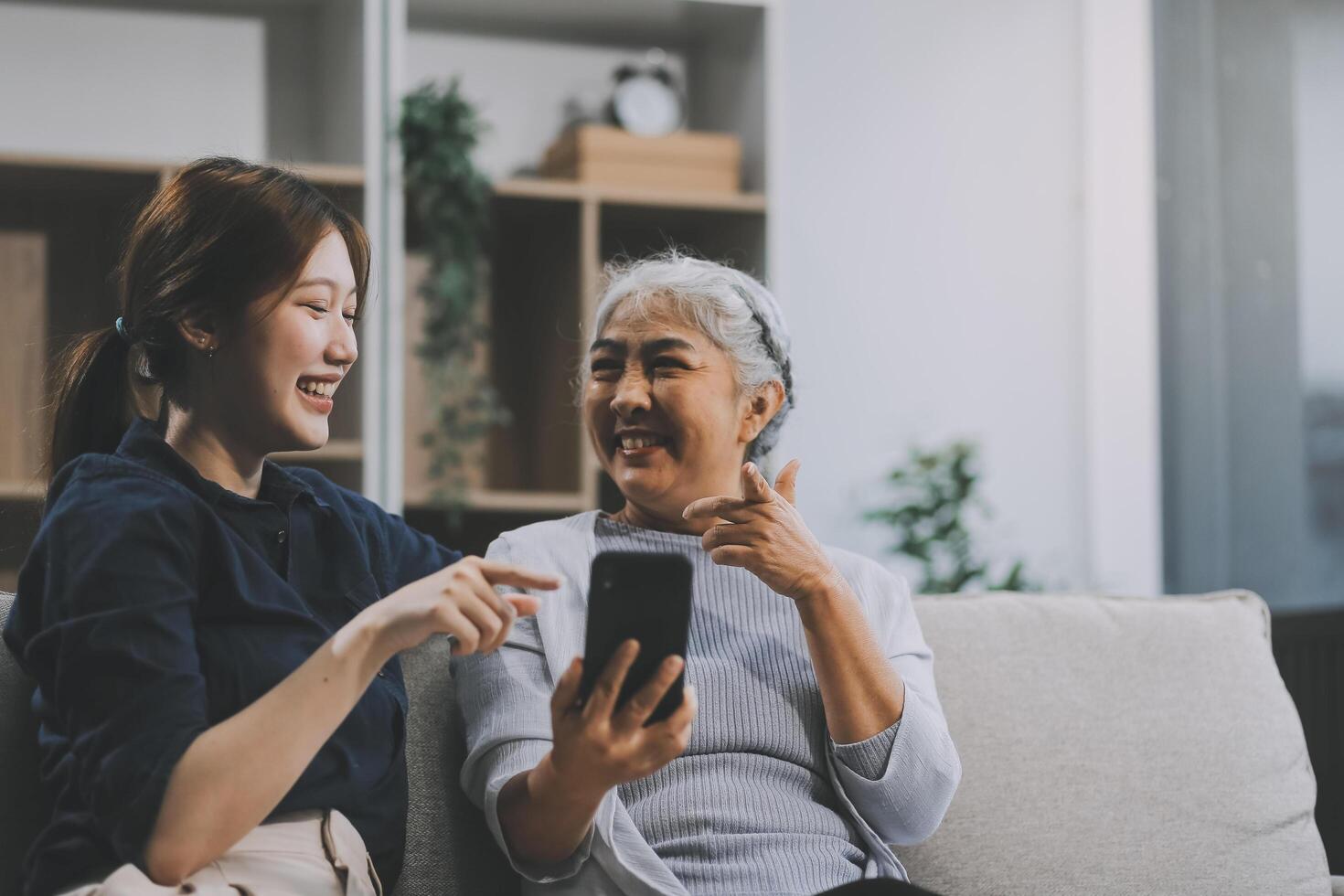 Cheerful mother and pretty teenager kid relaxing at cozy home, using mobile phone for Internet communication, resting on sofa with digital gadget, enjoying leisure, looking at camera photo