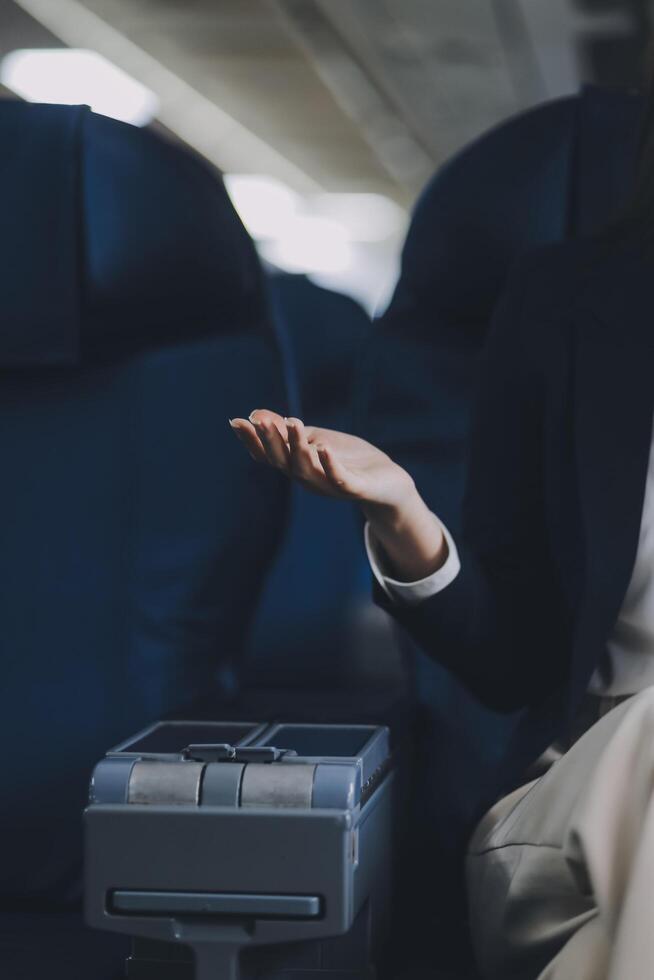A young Asian female airplane passenger sits by the window during the flight, holding her boarding pass, with her carry-on luggage stored overhead, wearing her seatbelt, and enjoying the journey. photo