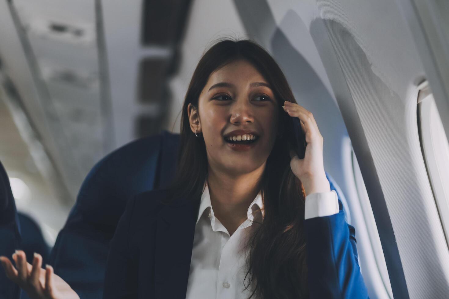 A young Asian female airplane passenger sits by the window during the flight, holding her boarding pass, with her carry-on luggage stored overhead, wearing her seatbelt, and enjoying the journey. photo